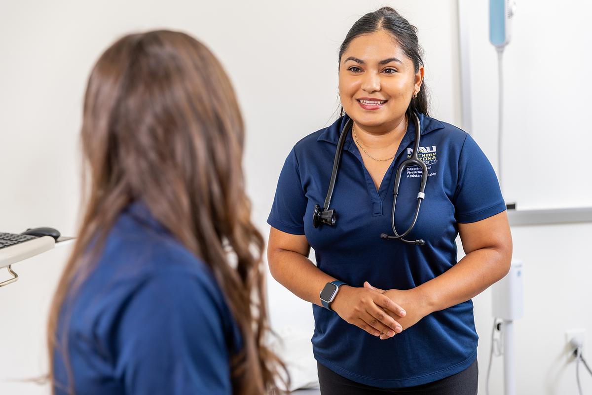 A healthcare professional wearing a stethoscope speaks to a patient in a clinical setting.
