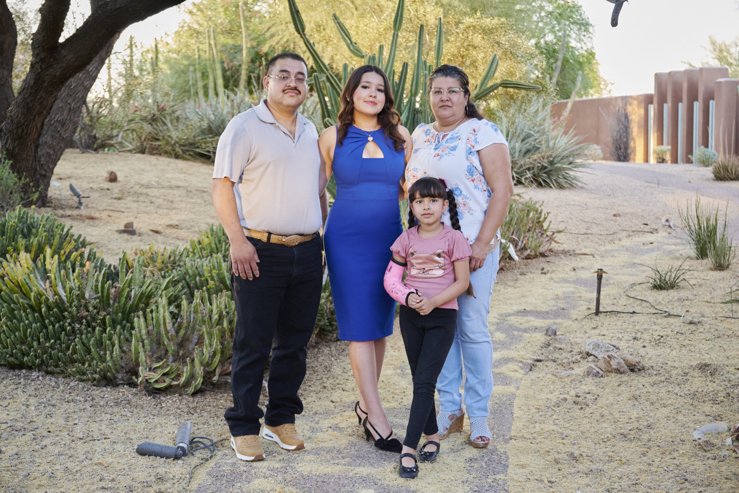 Four people, two adults and two children, stand together on a path in a desert-like garden with cacti and shrubs, posing for a photo.