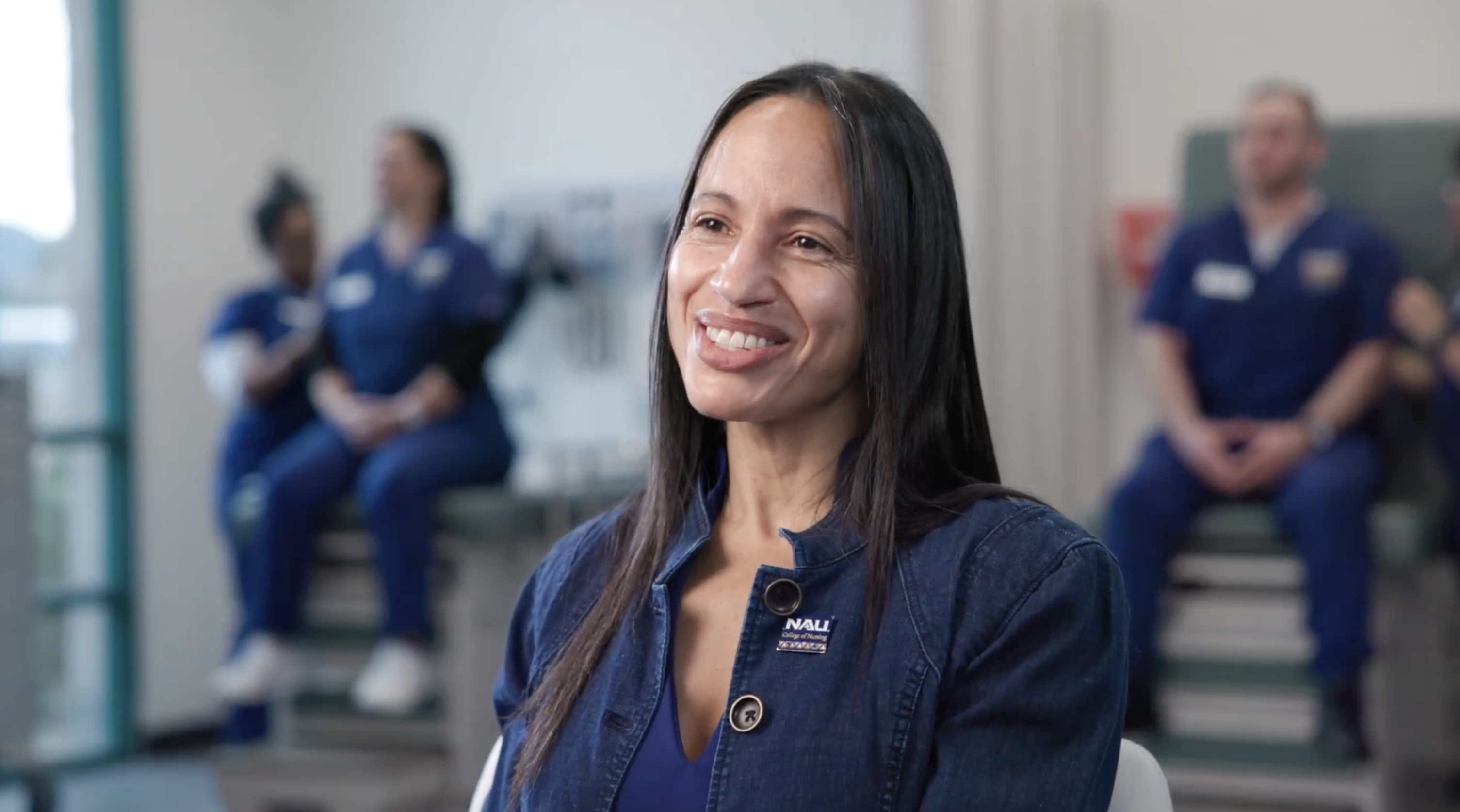 College of Nursing Dean Janina Johnson smiles at the camera wearing navy jacket with nursing students learning in the background