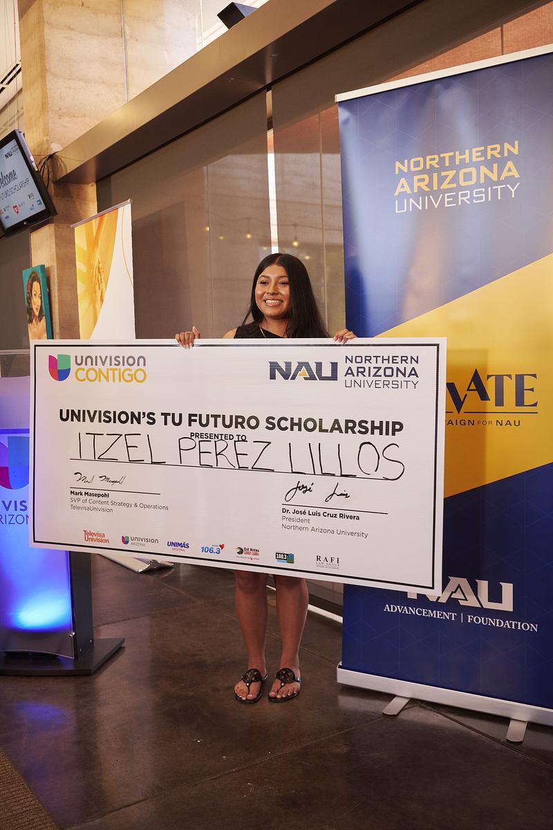 Itzel Perez Lillos holds a large check in front of a NAU banner announcing her as the Tu Futuro scholarship honoree